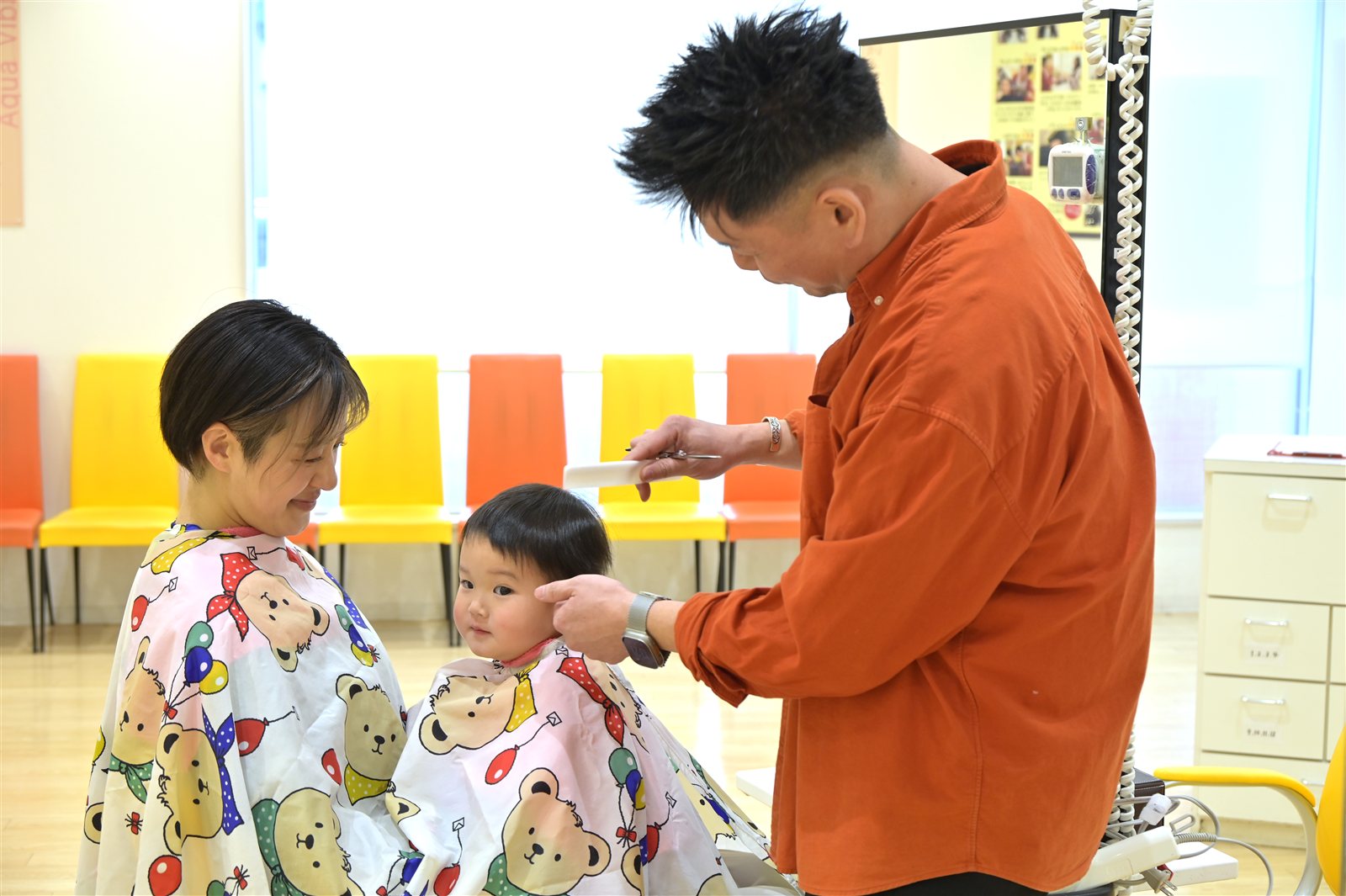 保護者のひざに座ったお子さまを美容師がカットする様子